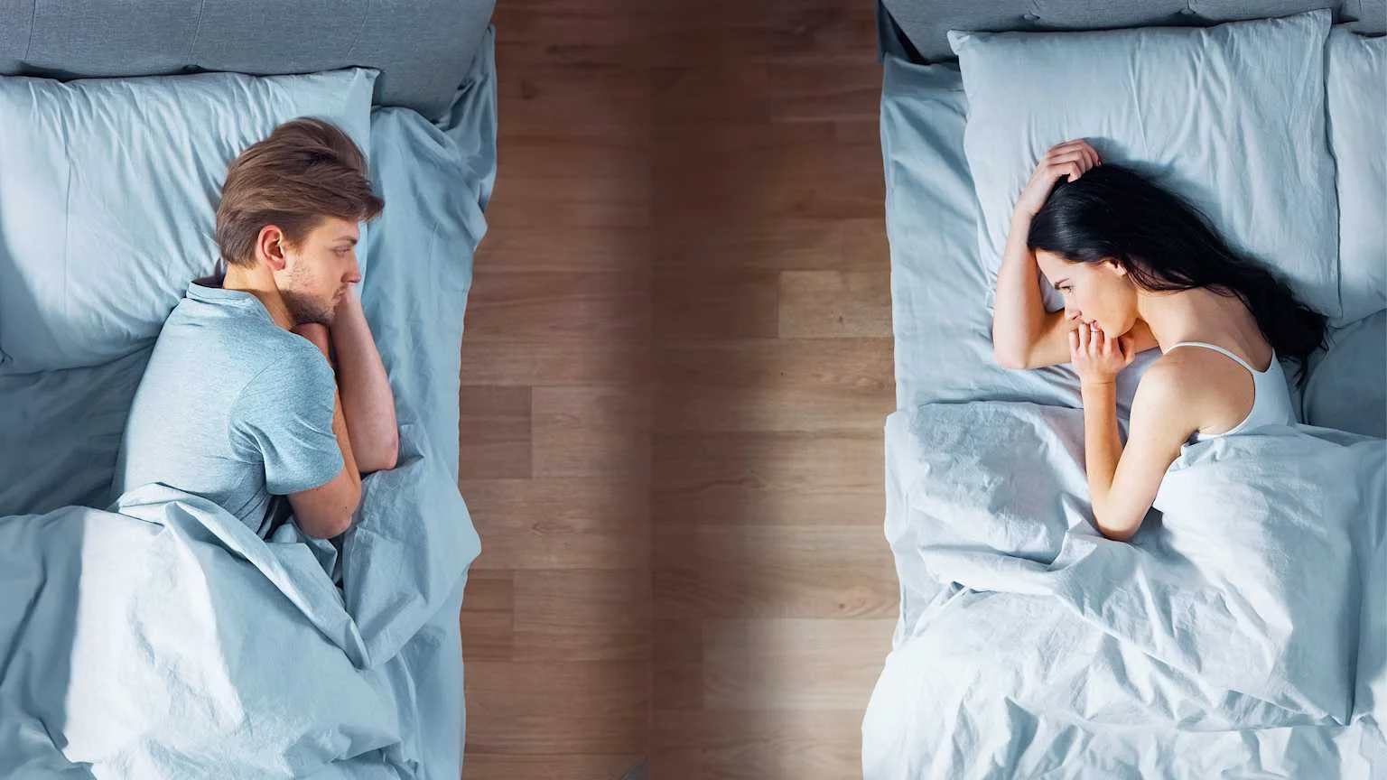 sleep divorce separate beds overhead — man and woman lying in individual single beds with gap between them showing intentional sleep separation
